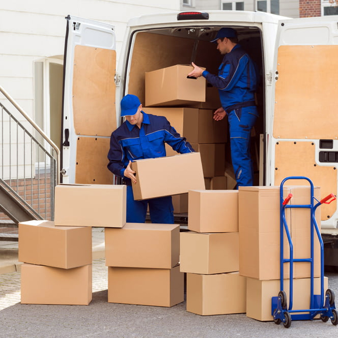 Two professional movers and packers in Dubai loading cardboard boxes into a moving van.